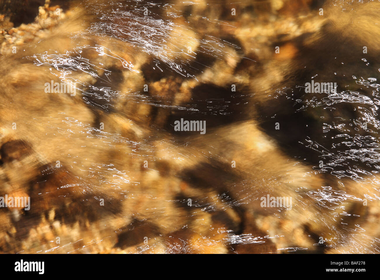 A close up of a section of a woodland stream with a stony bottom Light streaks in the water and plenty of movement blur Stock Photo