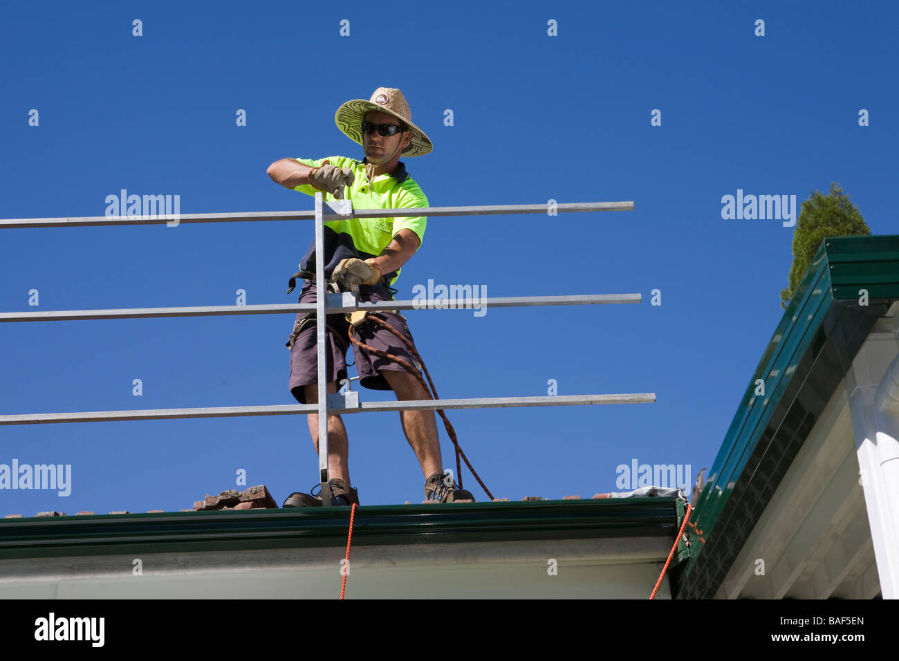 Man erecting safety rails around terra cotta tiled roof, Sydney, New