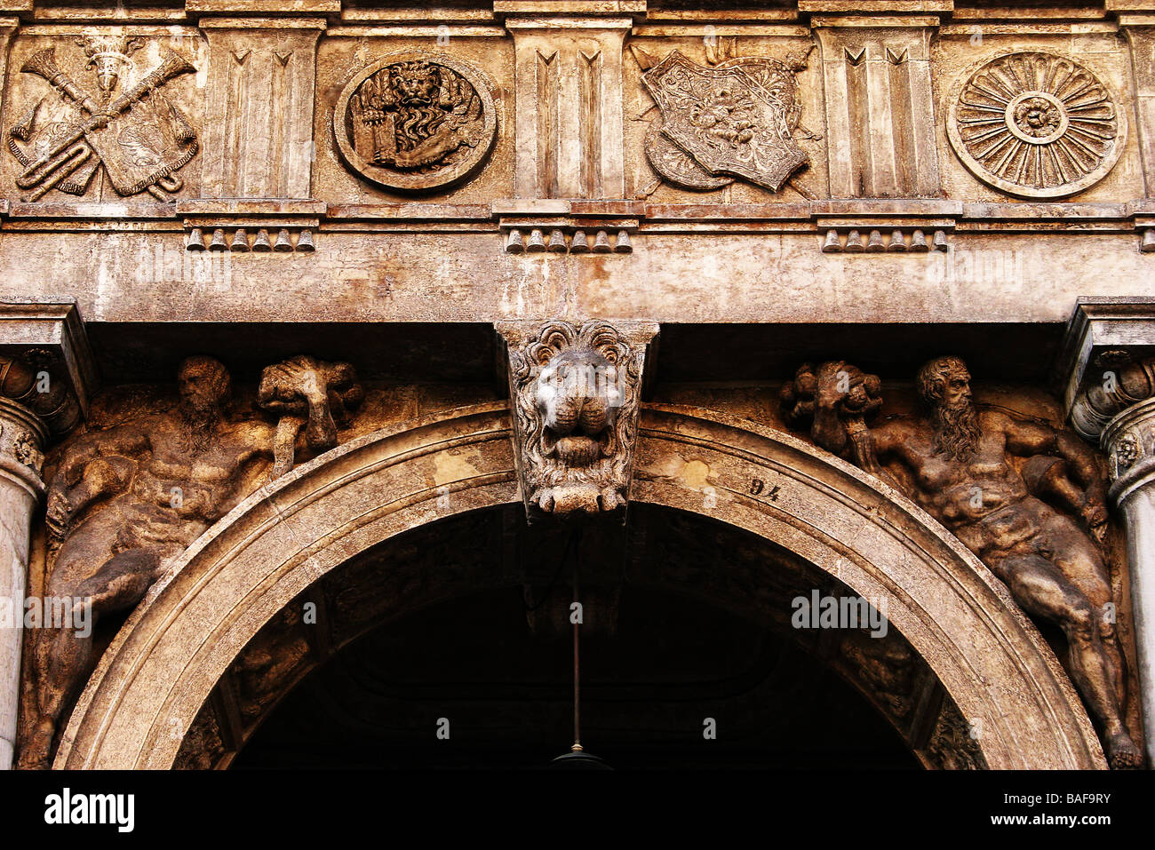 arch decorated with a lion's head and two male figures Venice
