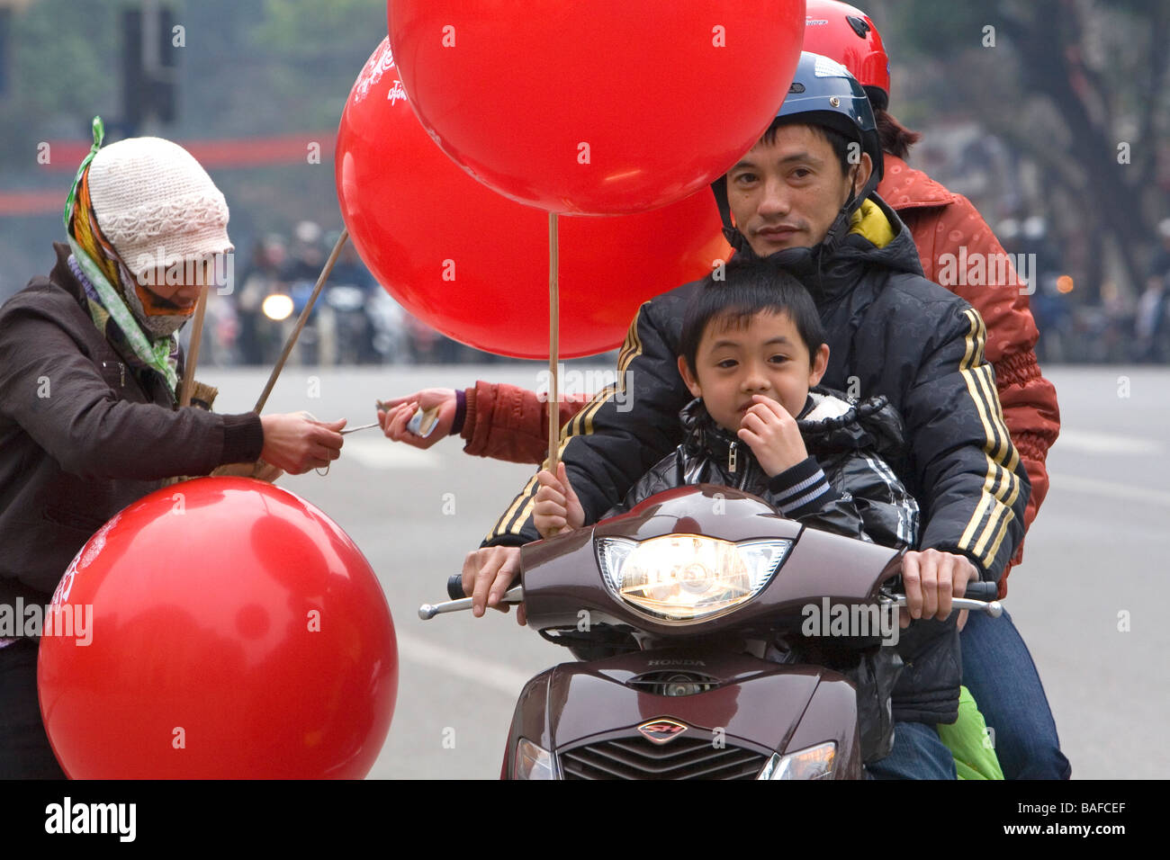 Vietnamese family on a motorbike purchase a balloon from a street vendor in Hanoi Vietnam Stock Photo