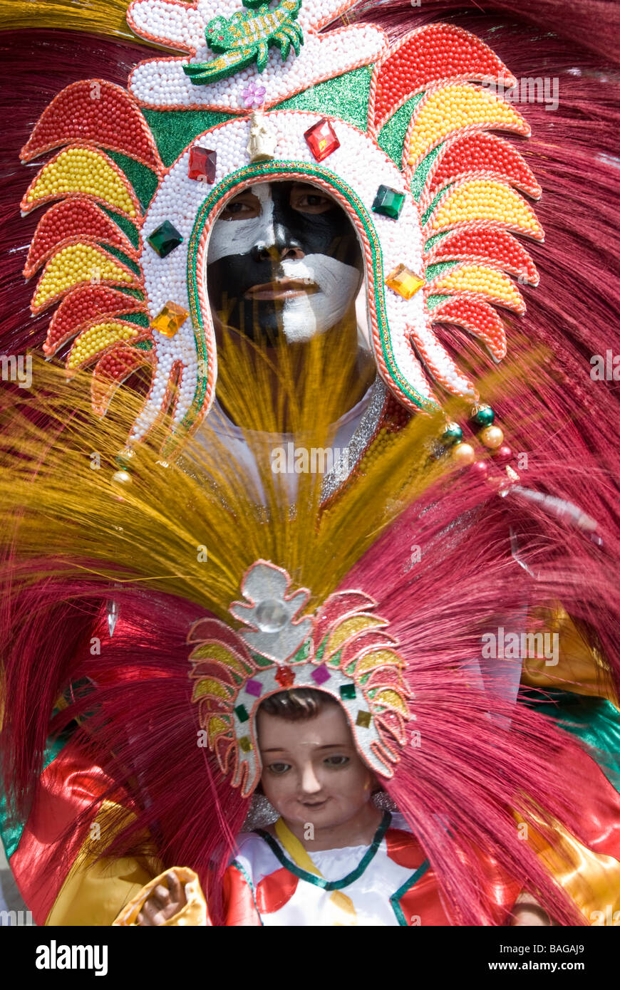 Person in chequered makeup and flamboyant costume, holding Santo Niño figure at Ati-Atihan festival in Kalibo, Philippines Stock Photo