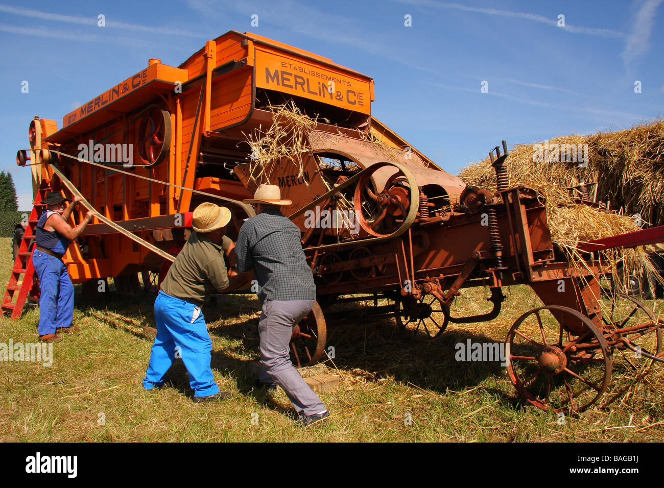 An old French belt driven threshing machine painted in orange in a