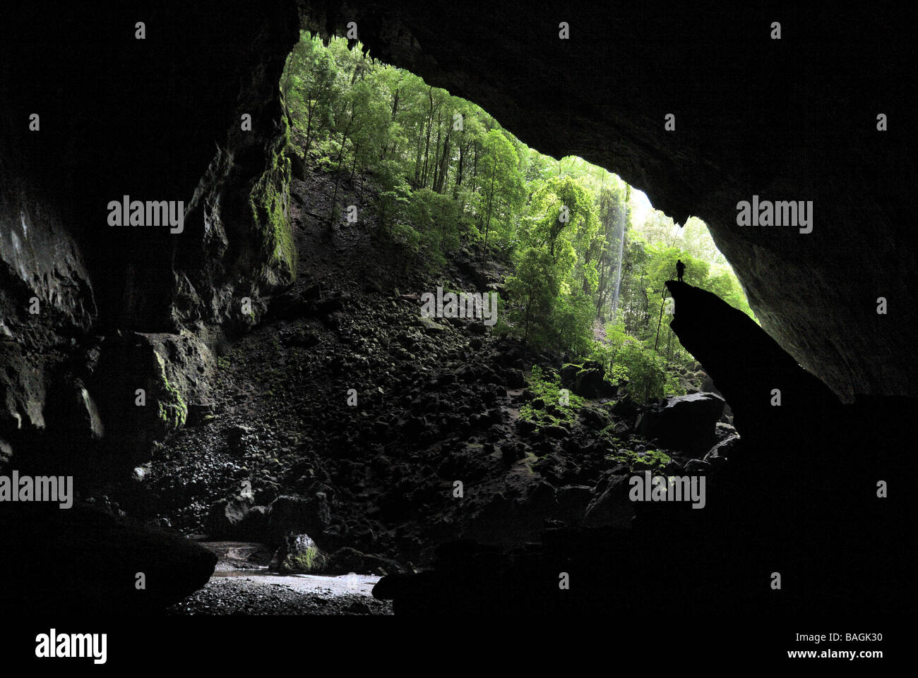 A lone cave explorer stands on a rock and looks out of the far entrance to Deer Cave, the largest passage in the world in Mulu Stock Photo