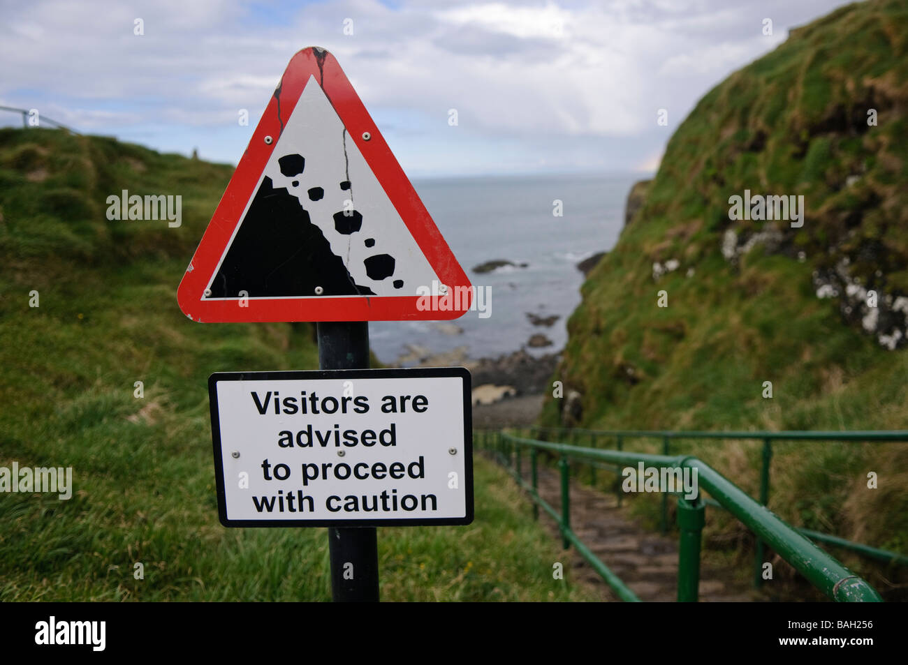 Falling rocks sign on a path beside a seaside cliff warning 'Visitors are advised to proceed with caution' Stock Photo