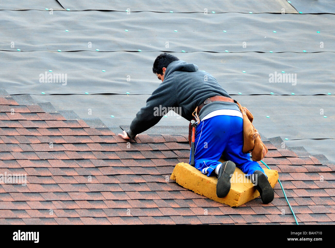 A Hispanic man applies shingles to the roof of a new house in Oklahoma City, Oklahoma, USA. Stock Photo