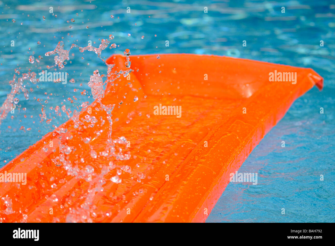 Splashed water over an orange air bed floating in a swimming pool. Stock Photo
