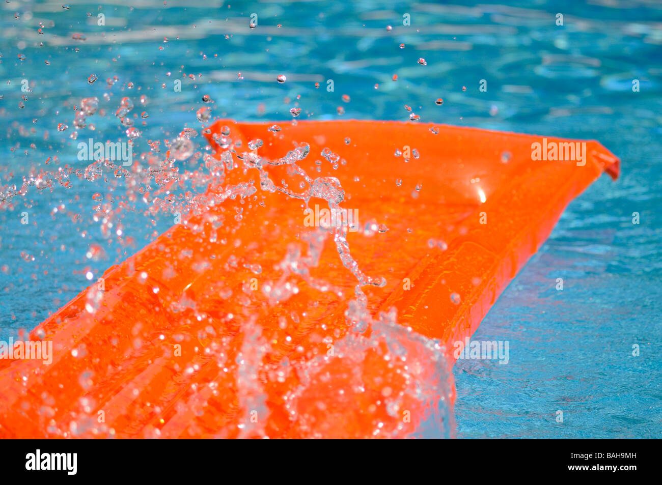 Splashed water over an orange air bed floating in a swimming pool Stock