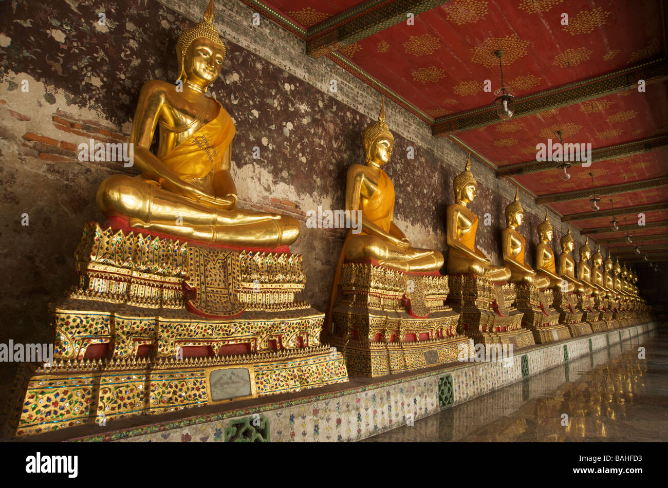 Gold Buddha statues line the galleries that encircle the main building at Wat Suthat in Bangkok Thailand Stock Photo