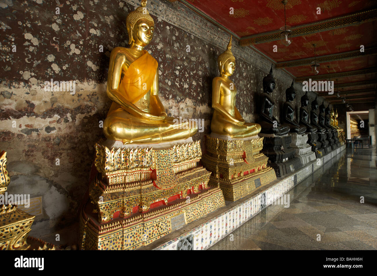 A row of black and gold Buddha statues line the galleries at Wat Suthat temple in Bangkok Thailand Stock Photo