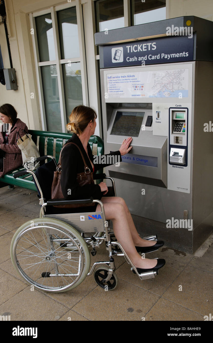Woman in a wheelchair purchasing a railway ticket from a automated