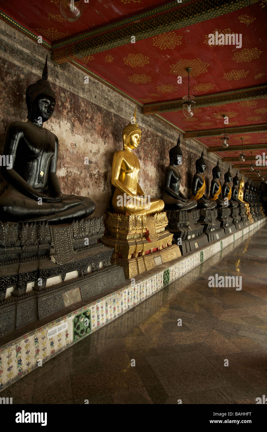 A row of black and gold Buddha statues line the galleries at Wat Suthat temple in Bangkok Stock Photo