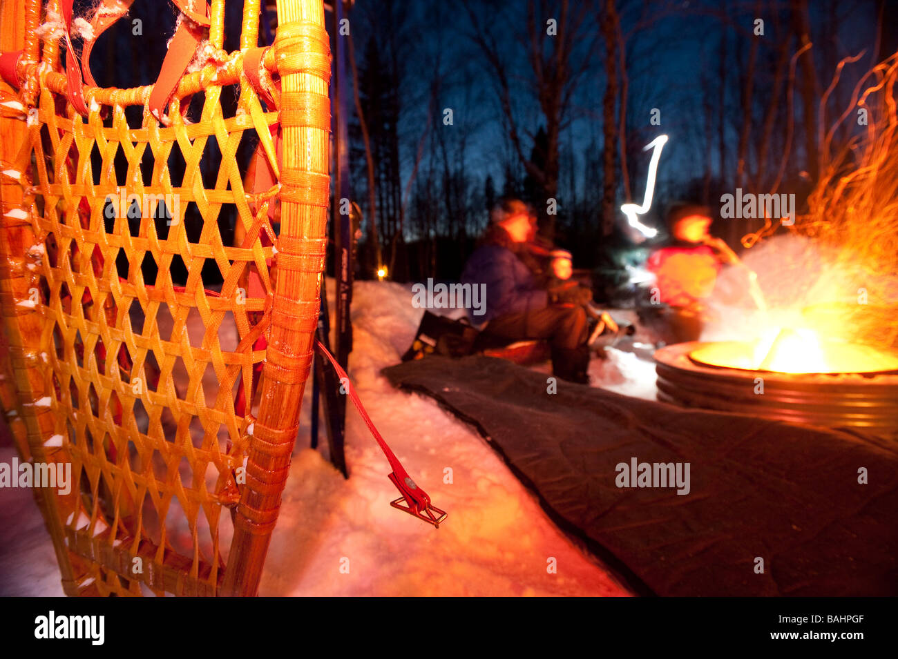 PEOPLE TAKE A BREAK FROM NIGHT SKIING AND SNOWSHOEING TO WARM UP NEXT TO A FIRE Stock Photo