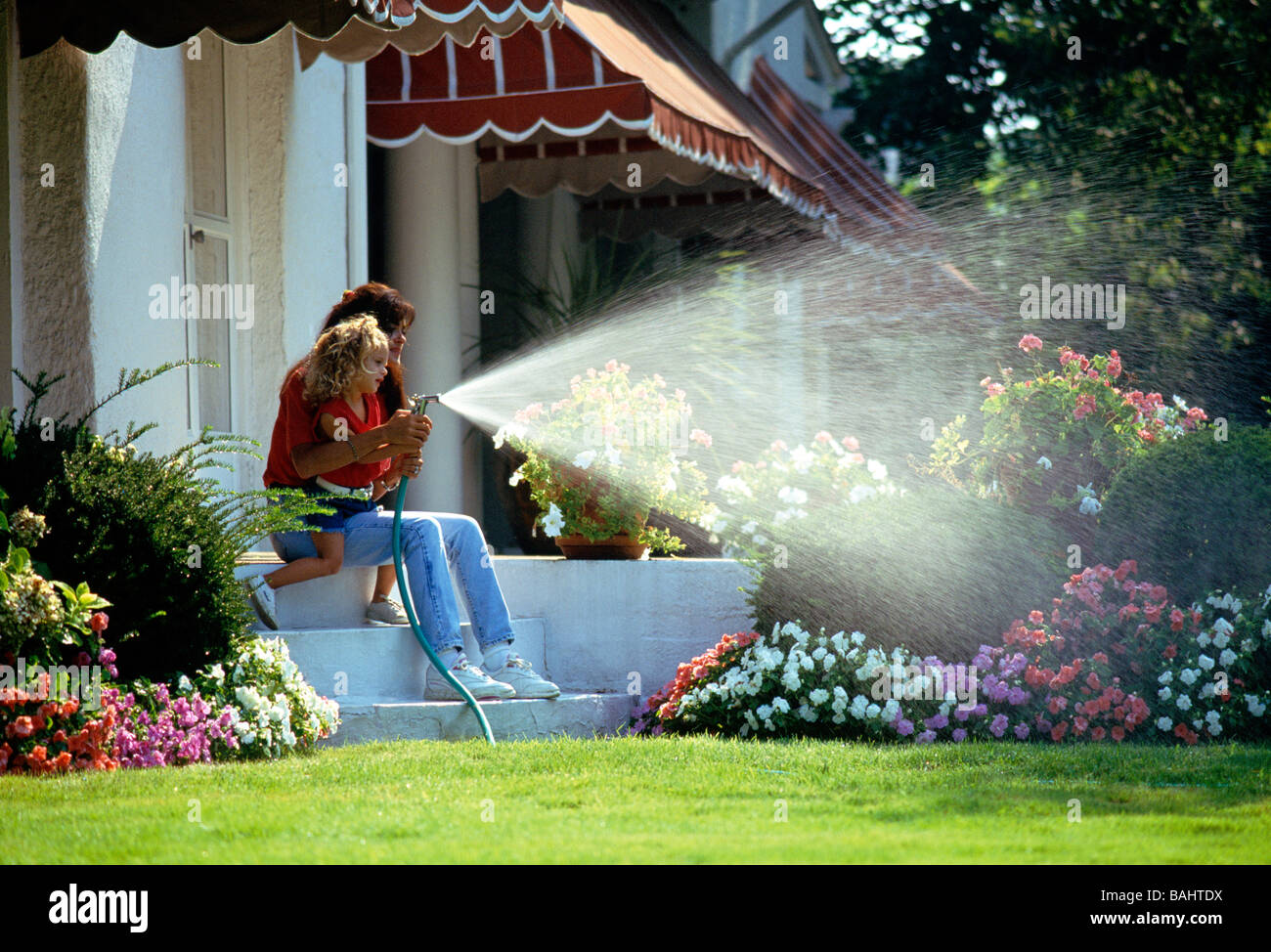 Mother and young daughter using a garden hose to water flower beds on