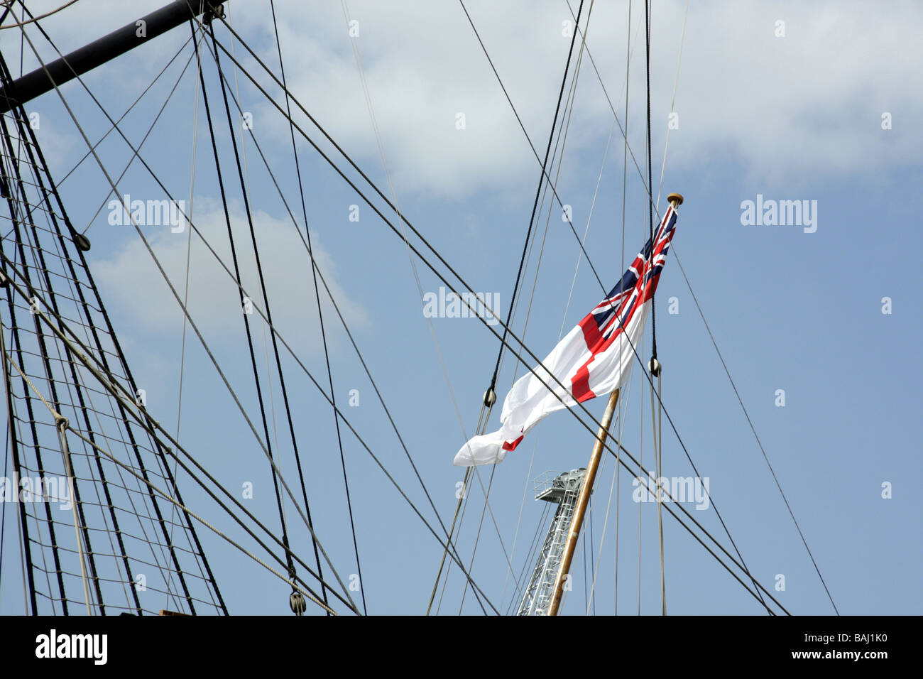Royal Navy White Ensign flag flying against a blue sky with ship rigging in the background Stock Photo