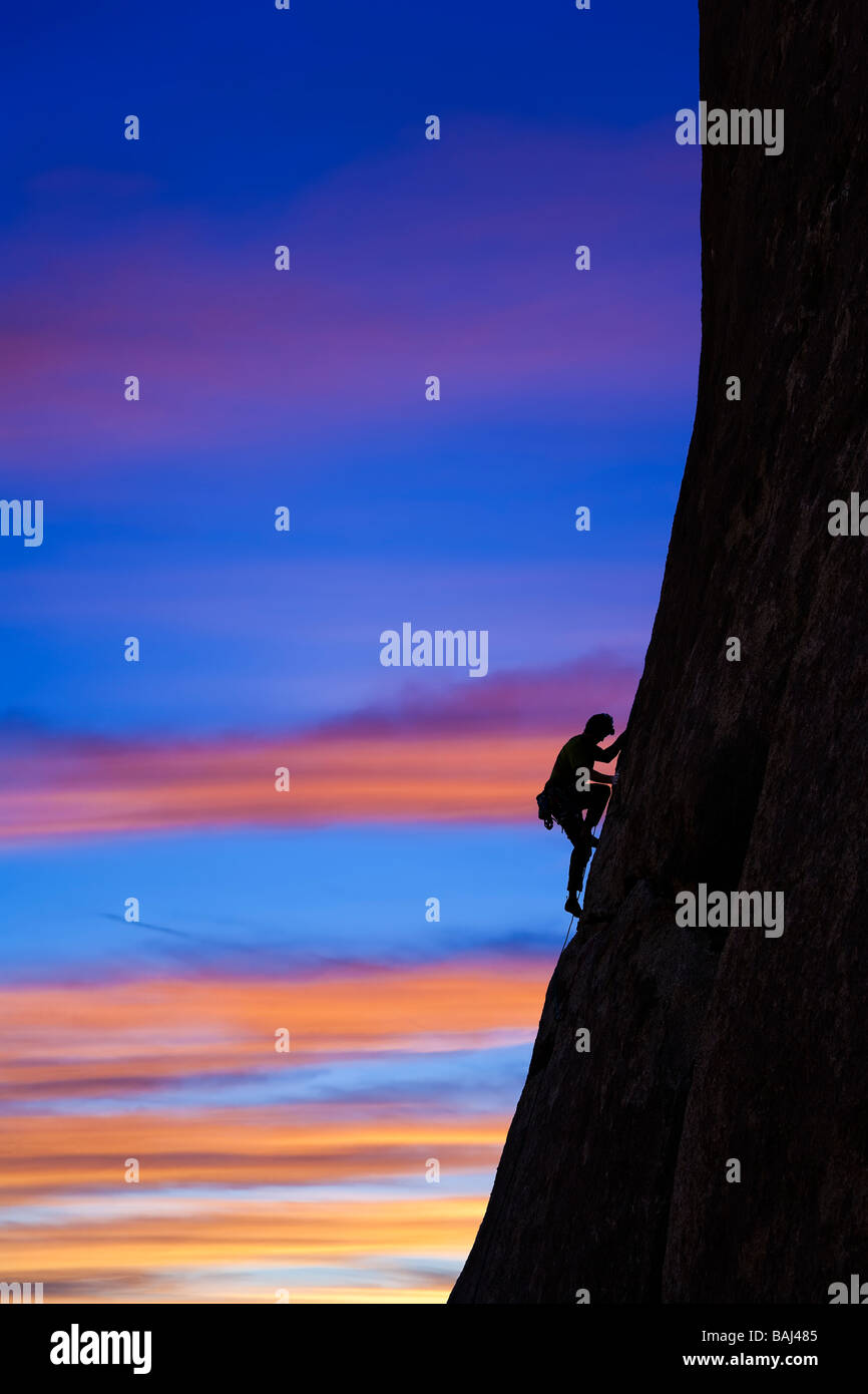 A climber is silhouetted as he clings to a steep rock face in Joshua Tree National Park California Stock Photo