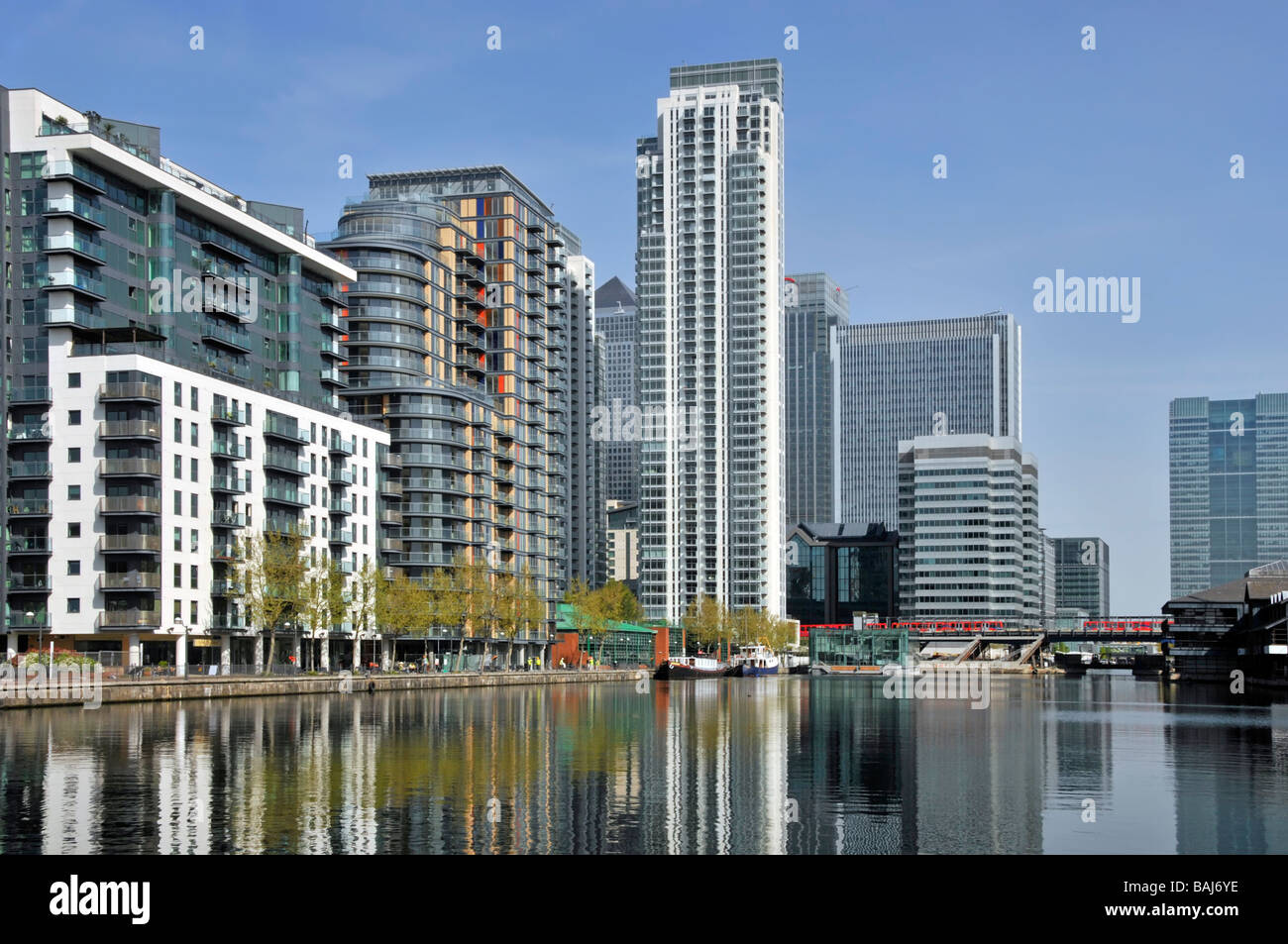 East London Docklands waterside housing in high rise apartments flats development water reflections Millwall Docks Canary Wharf & DLR train beyond UK Stock Photo