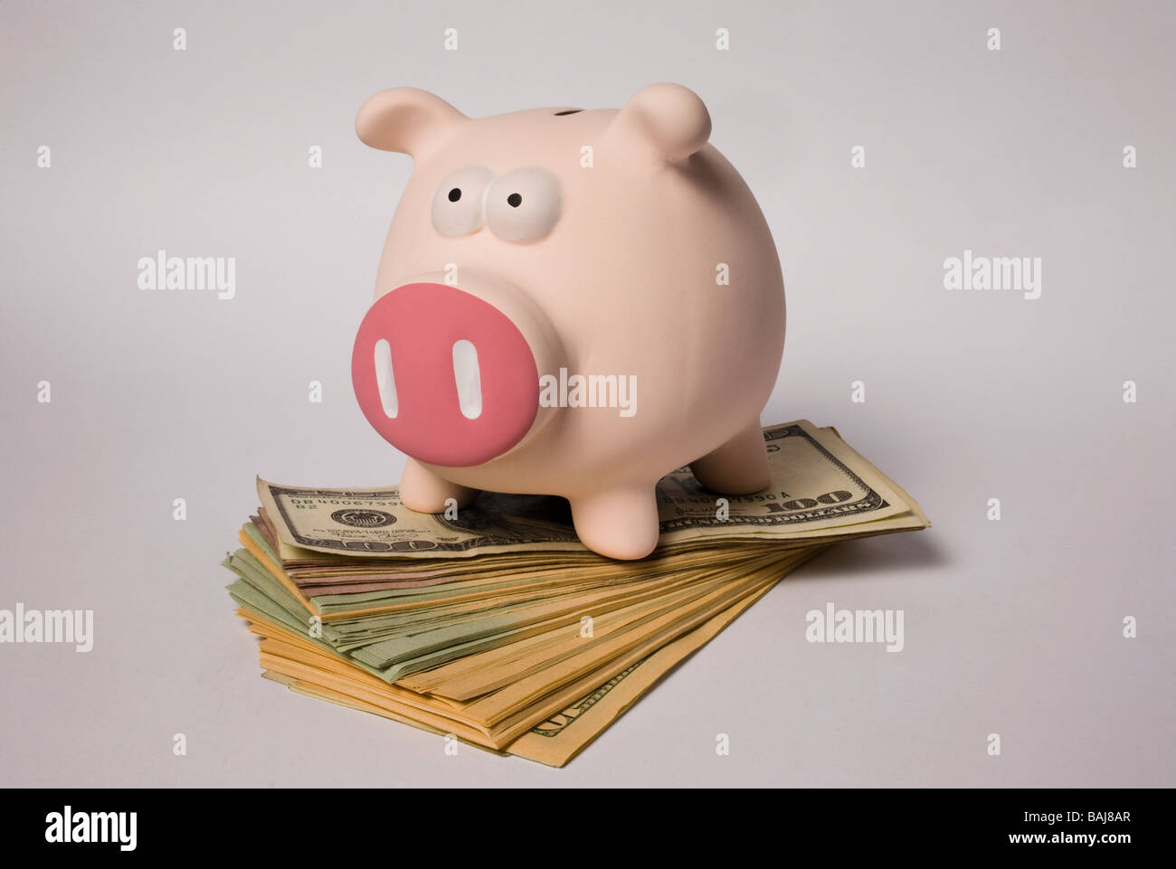 pink coloured piggy bank standing on a pile of US dollars of various denominations Stock Photo