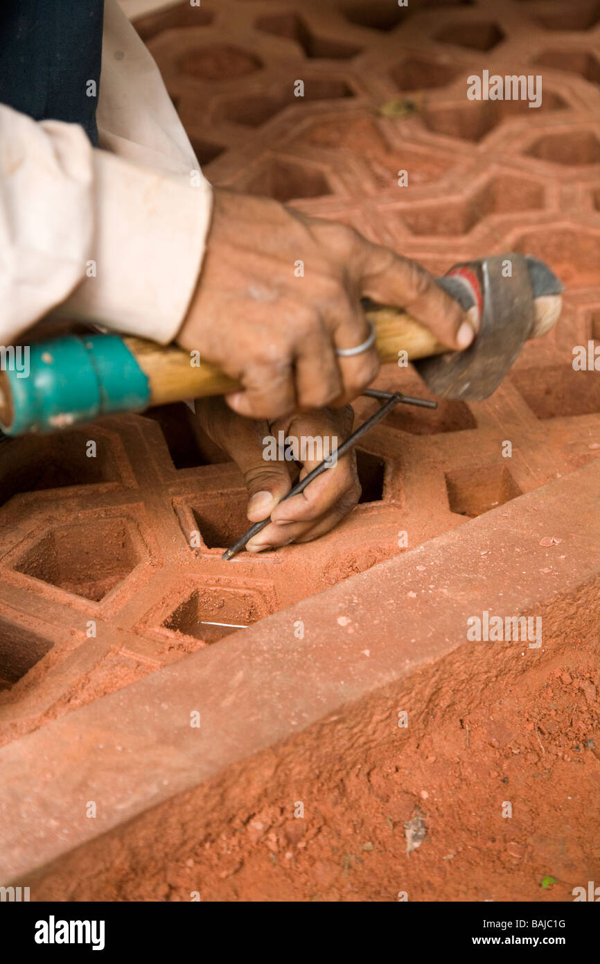 An Indian stone mason chisels a detailed stone screen at the site of