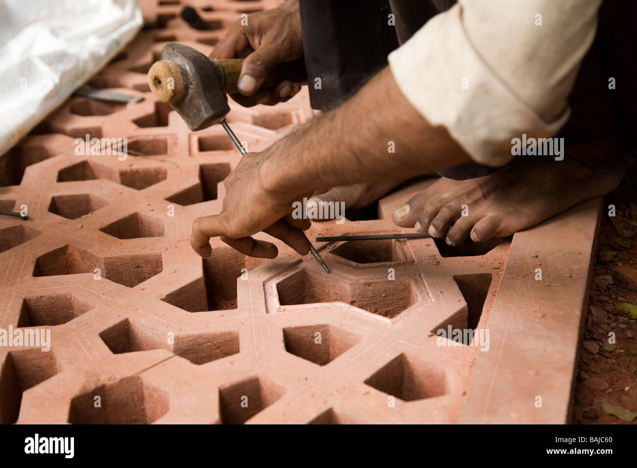 An Indian stone mason chisels a detailed stone screen at the site of