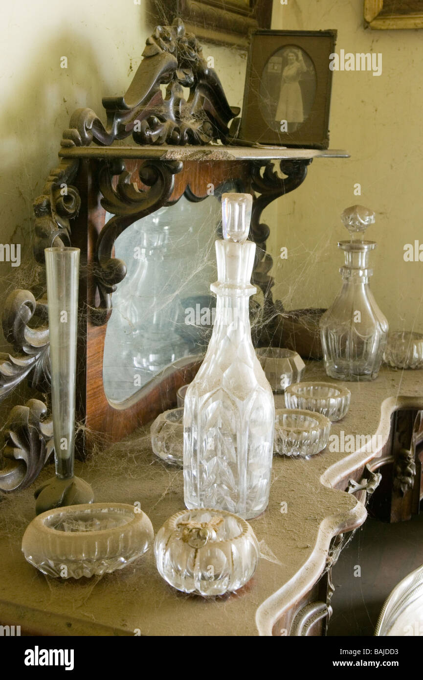 A sideboard with glass decanters and other ornaments covered in a thick layer of dust in a room not dusted for more than 20 year Stock Photo