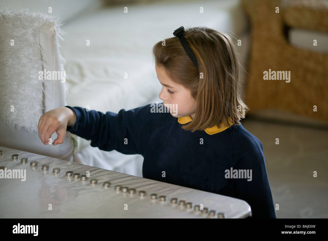 young school girl looking thoughtful counting out money into piles of coins at home Stock Photo