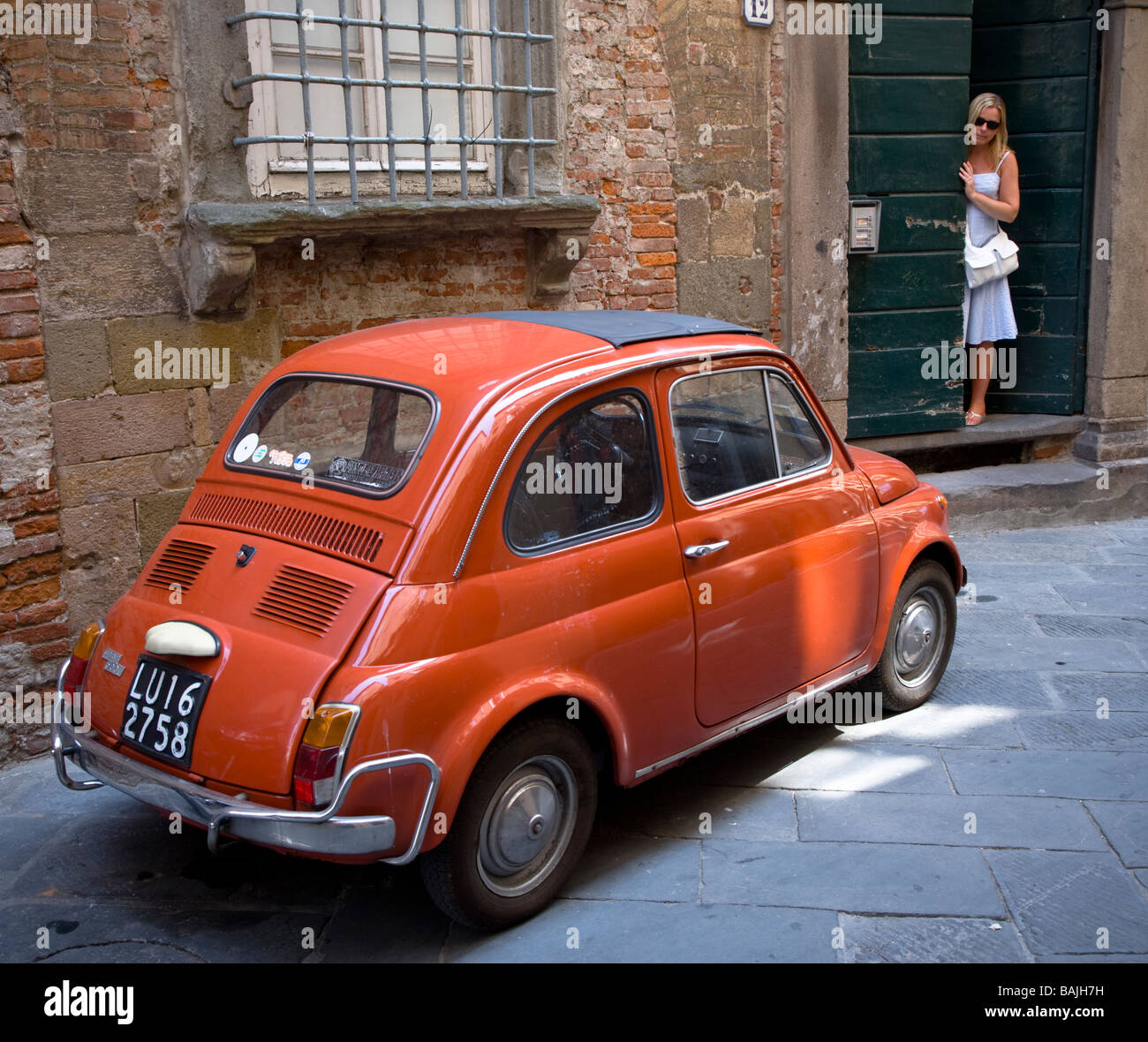 An attractive blond woman in a doorway & an orange Fiat 500 in an ...