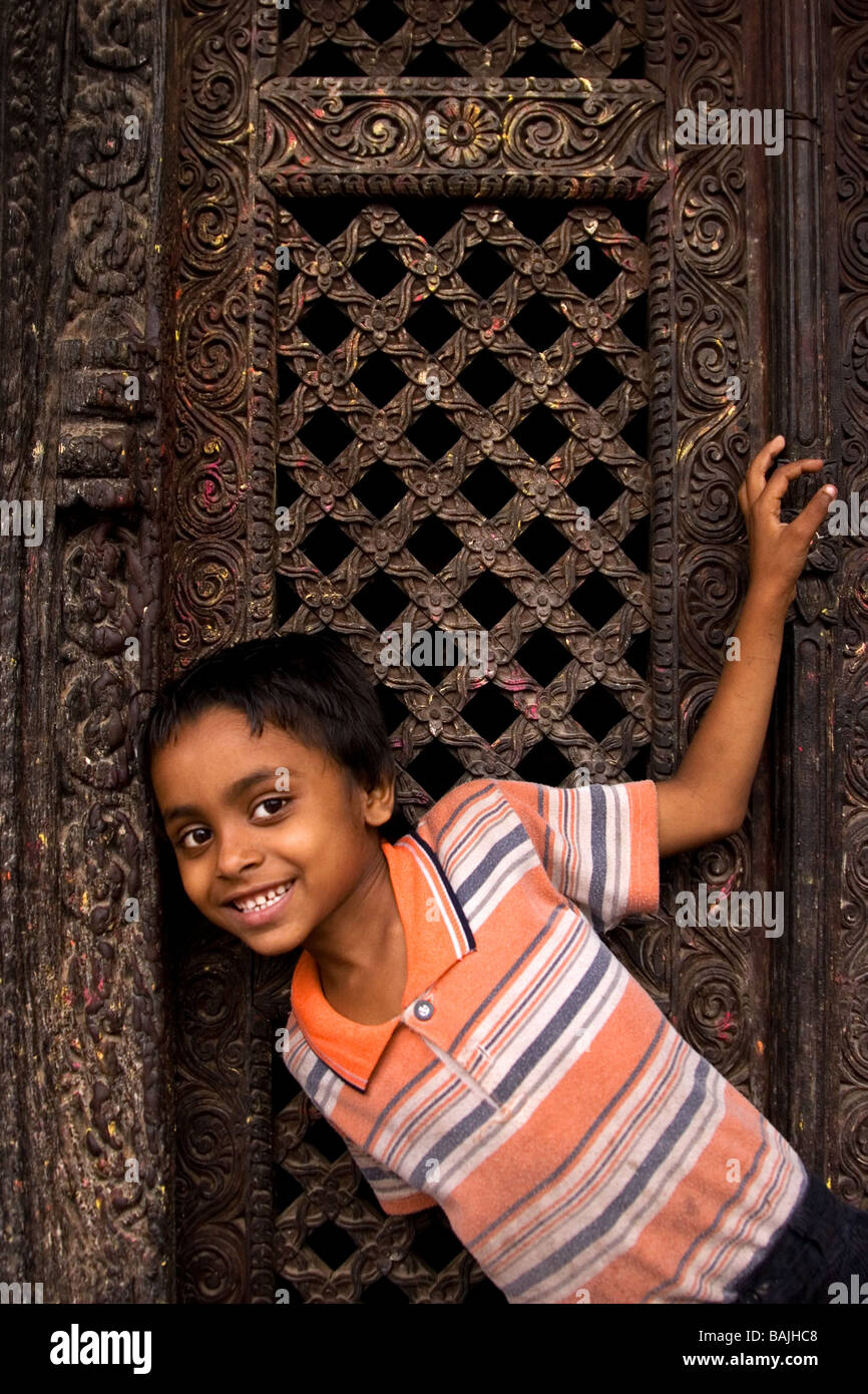 Small Nepali Boy Leans into Shot at Traditional-Carved Wood Temple Door, Durbar Square, Bhaktapur, Kathmandu Valley Stock Photo