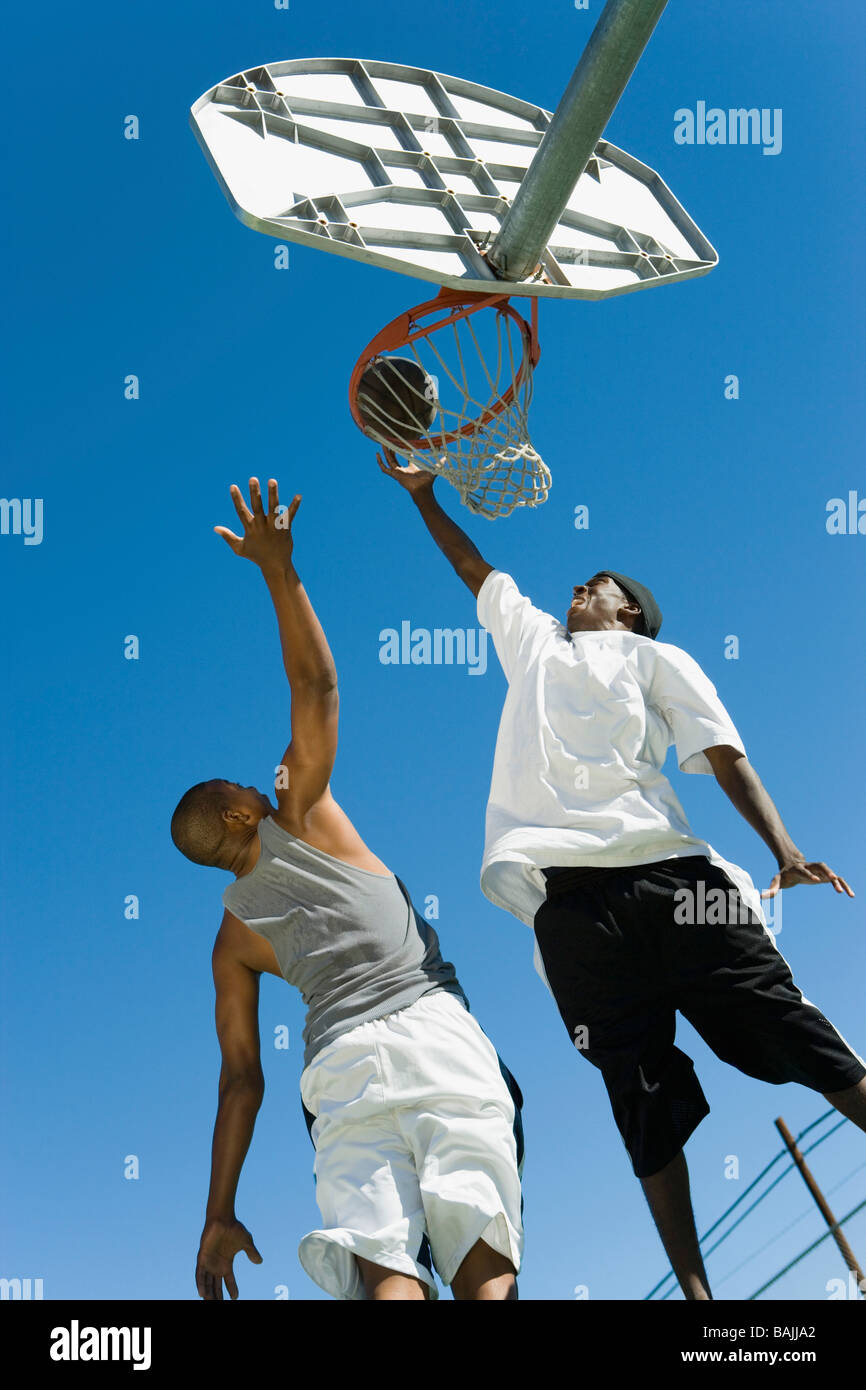Basketball player guarding another as he shoots basketball, low angle