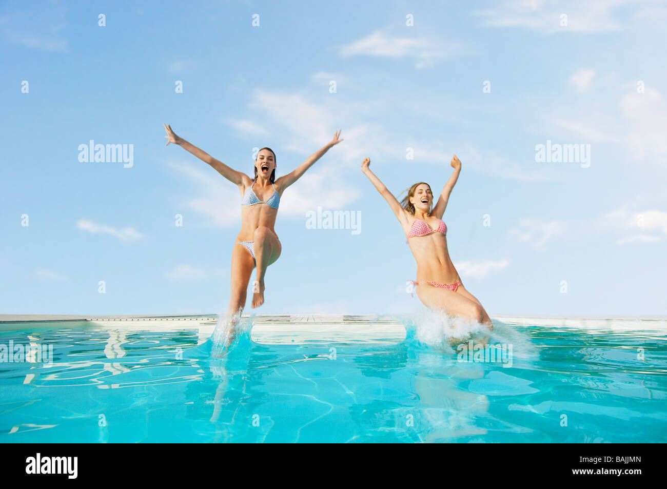 Young Women Jumping into Swimming Pool, front view Stock Photo