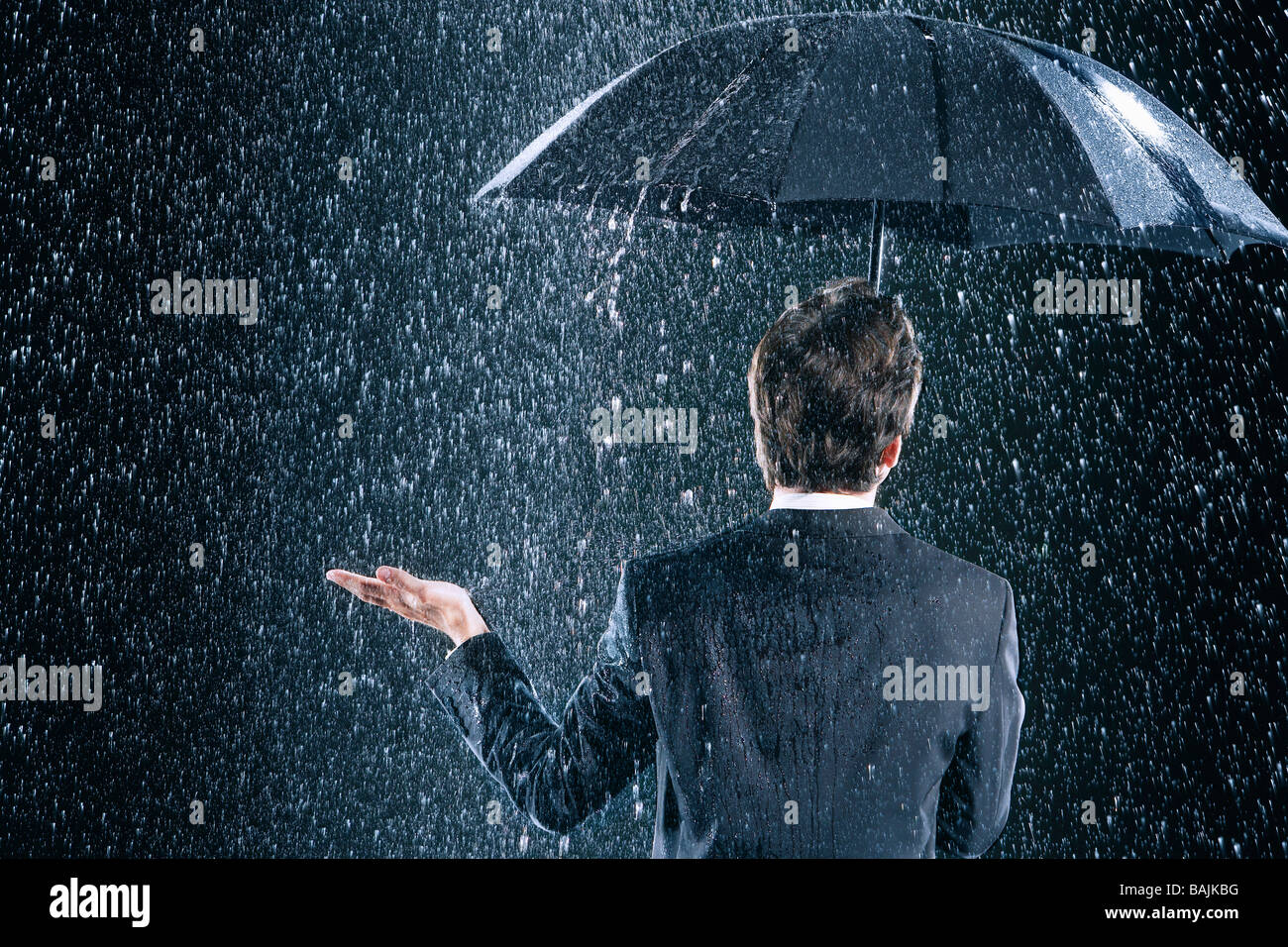 Businessman staying dry under umbrella during downpour, back view Stock Photo