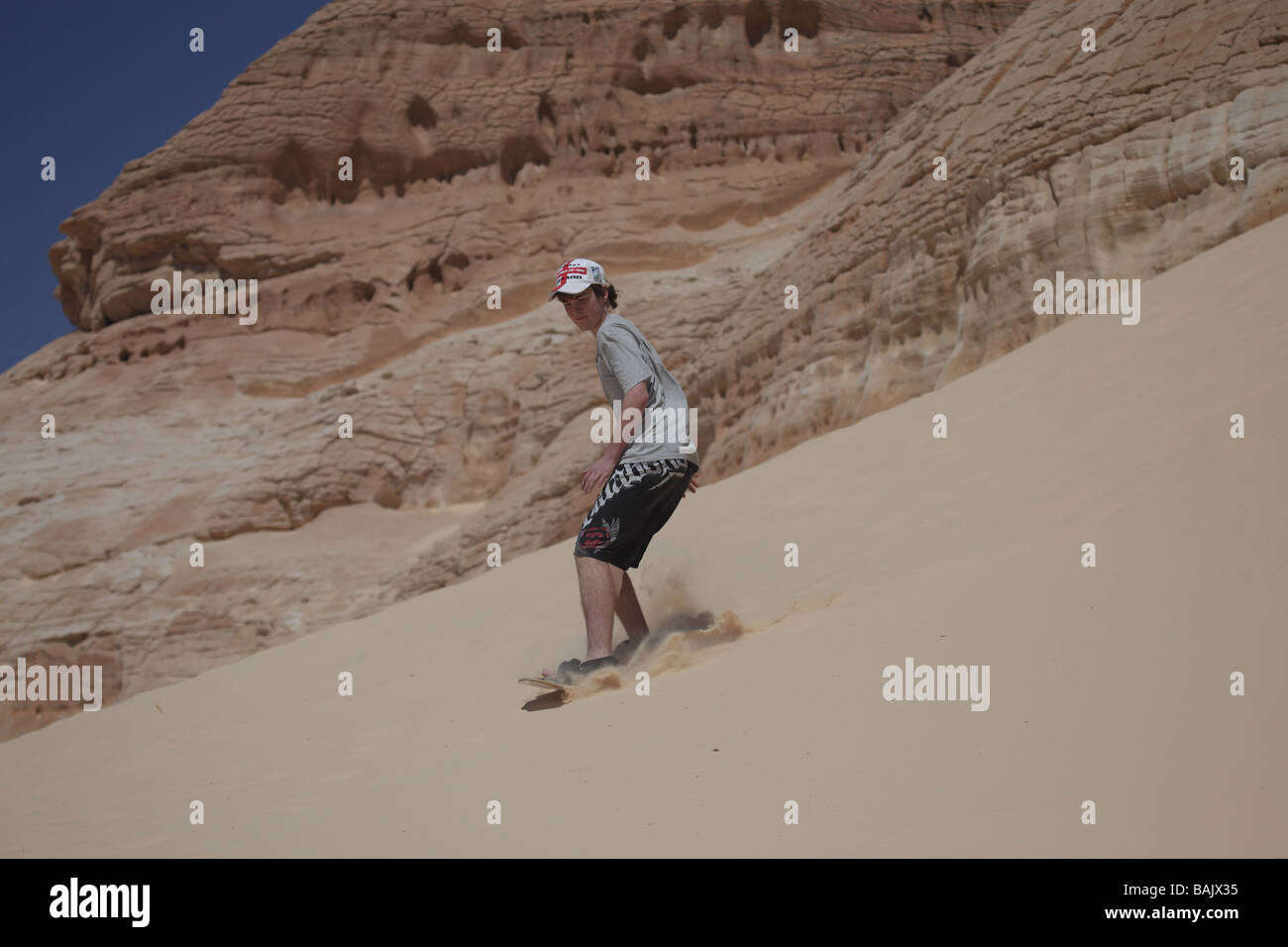 young teenage boy sand boarding down dune in the Sinai desert with mountain rocks in the background Stock Photo