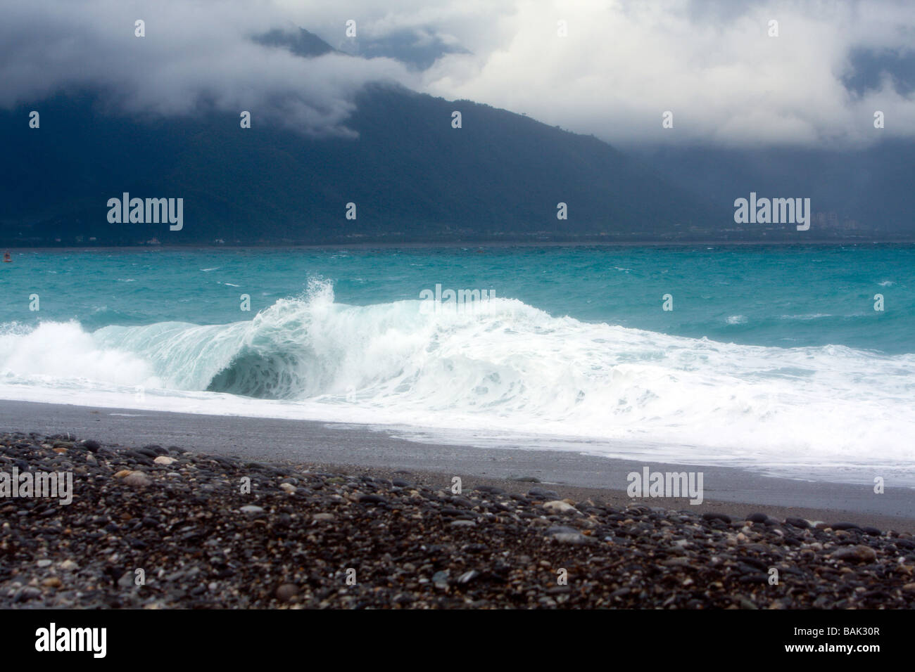 Central Mountain Range behind plunging or dumping wave, view from pebble beach during rainy day along Chisingtan Scenic Area, Hualien, Taiwan Stock Photo