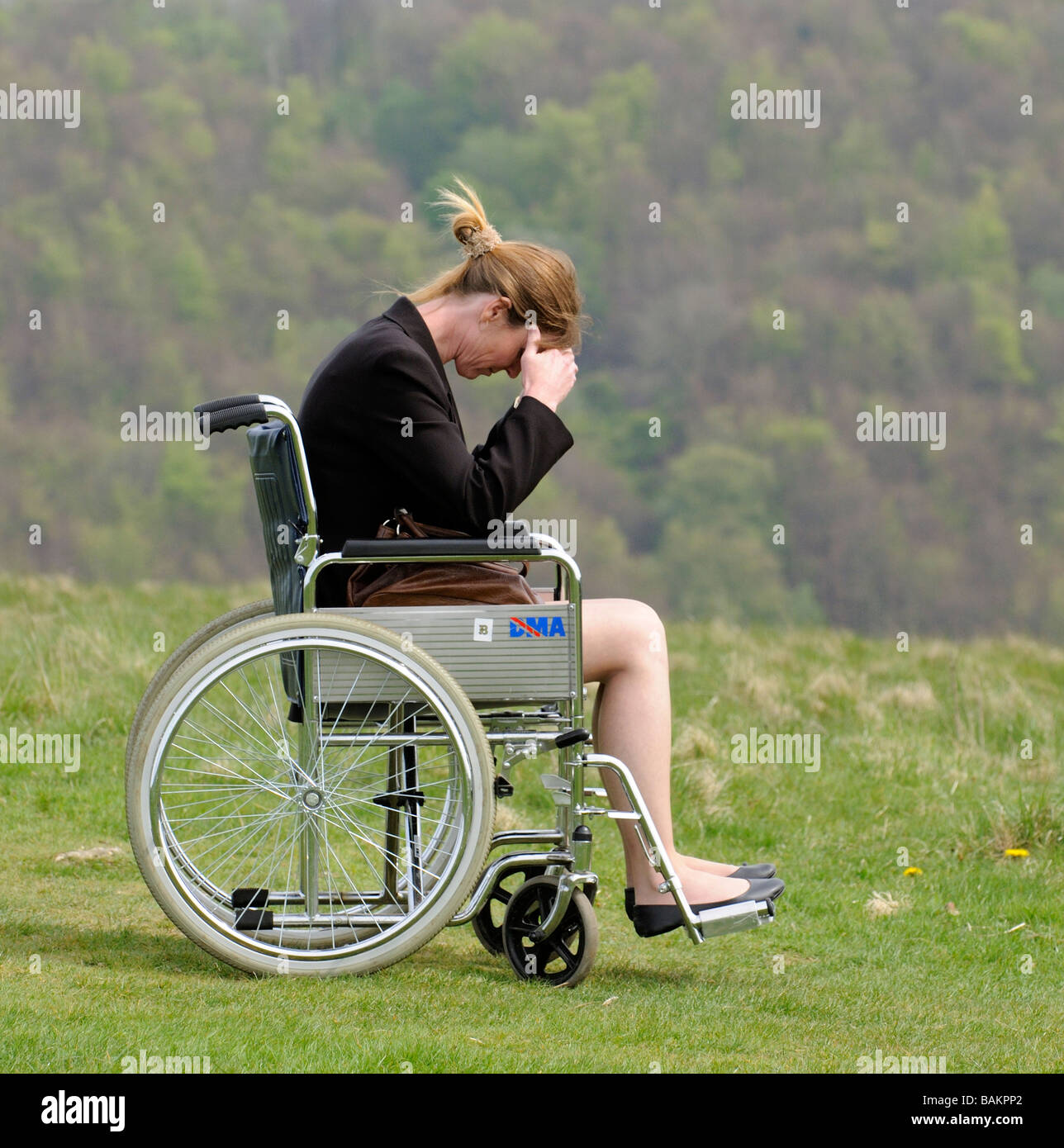 woman with head in hands sitting in a self propel dma wheelchair overlooking english countryside Stock Photo