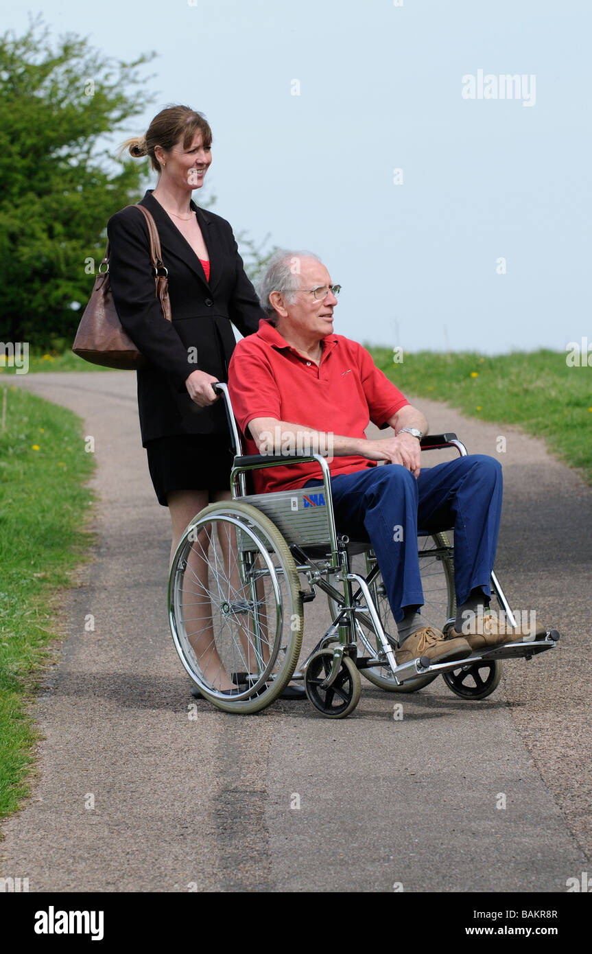 Male invalid wheelchair user and female carer pushing the chair England UK Stock Photo