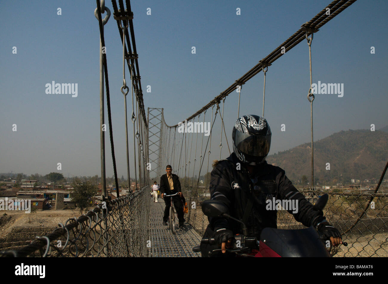 motorcycle croses a narrow suspension bridge in asia Stock Photo