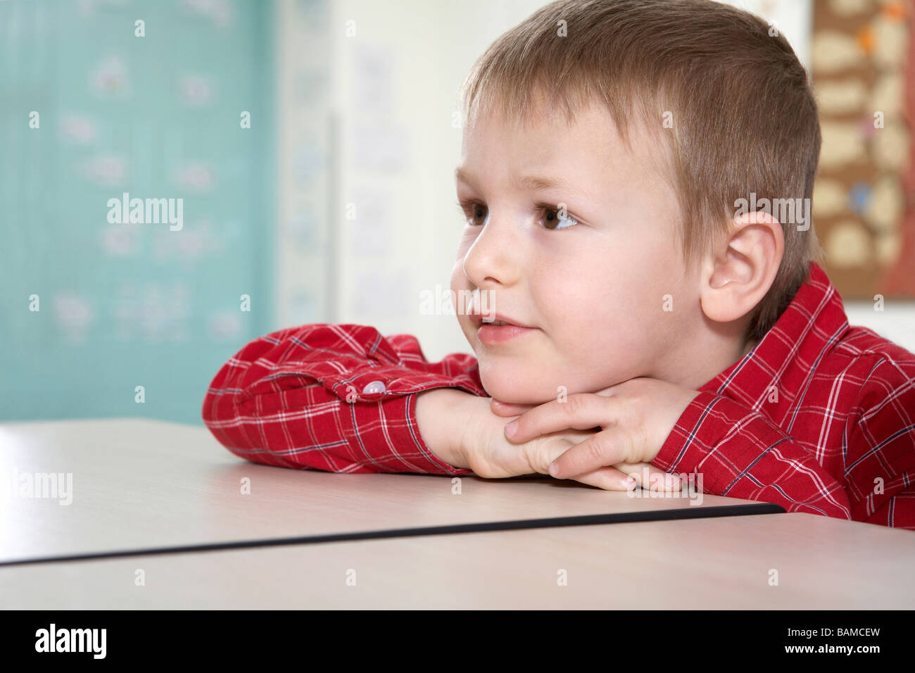 Boy Sitting At Desk, Looking Into Distance Stock Photo