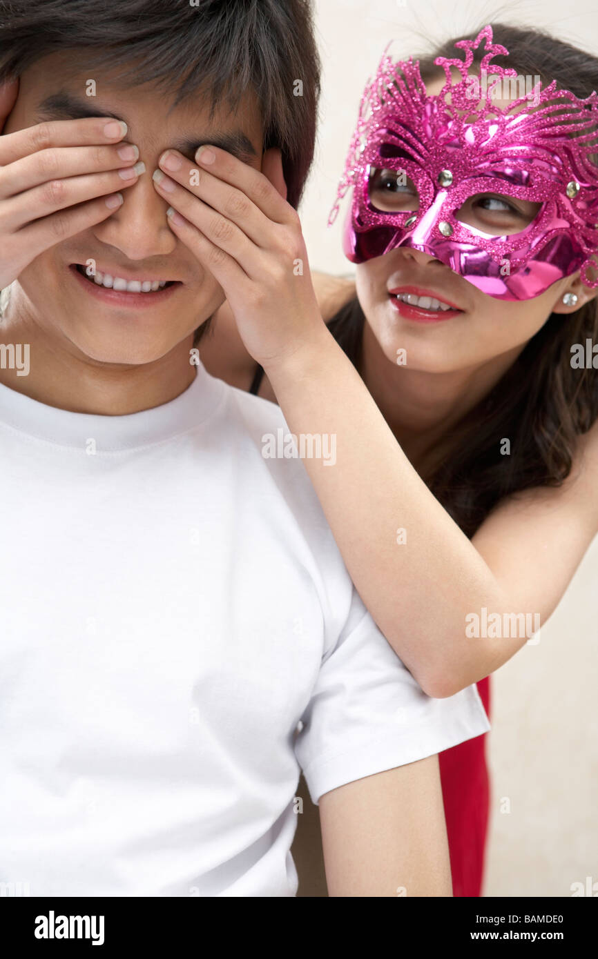 Young Woman Wearing Masquerade Mask Covering Young Man's Eyes Stock Photo