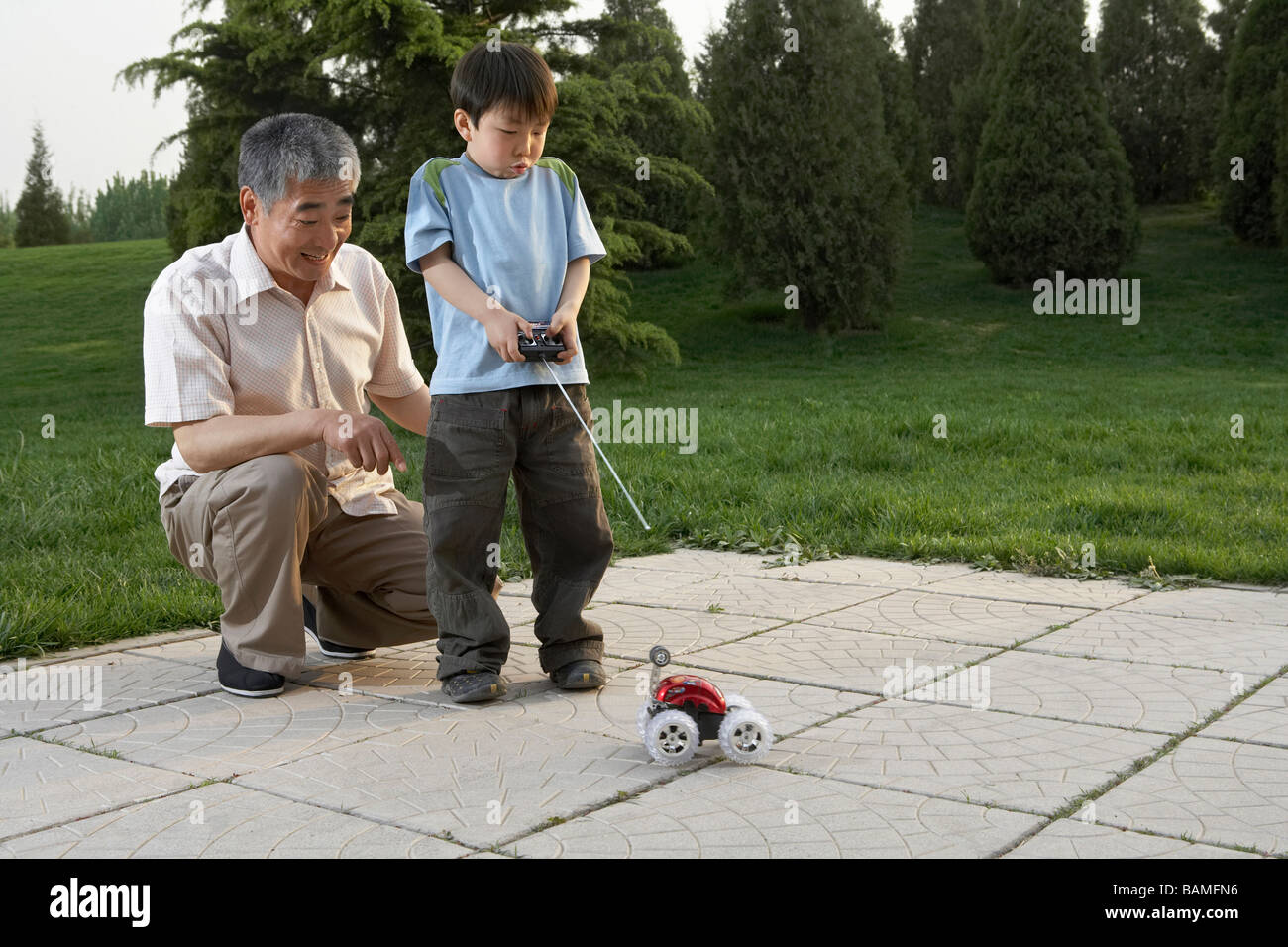 Grandfather And Grandson With A Remote Control Car In The Park Stock Photo