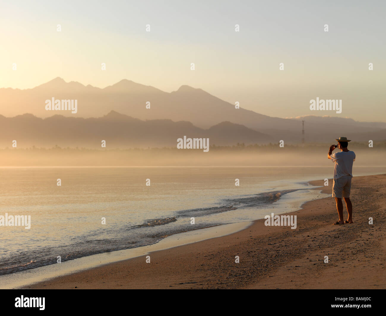 A man takes a photo of the rising sun over the Java Sea in Lombok Indonesia. Stock Photo