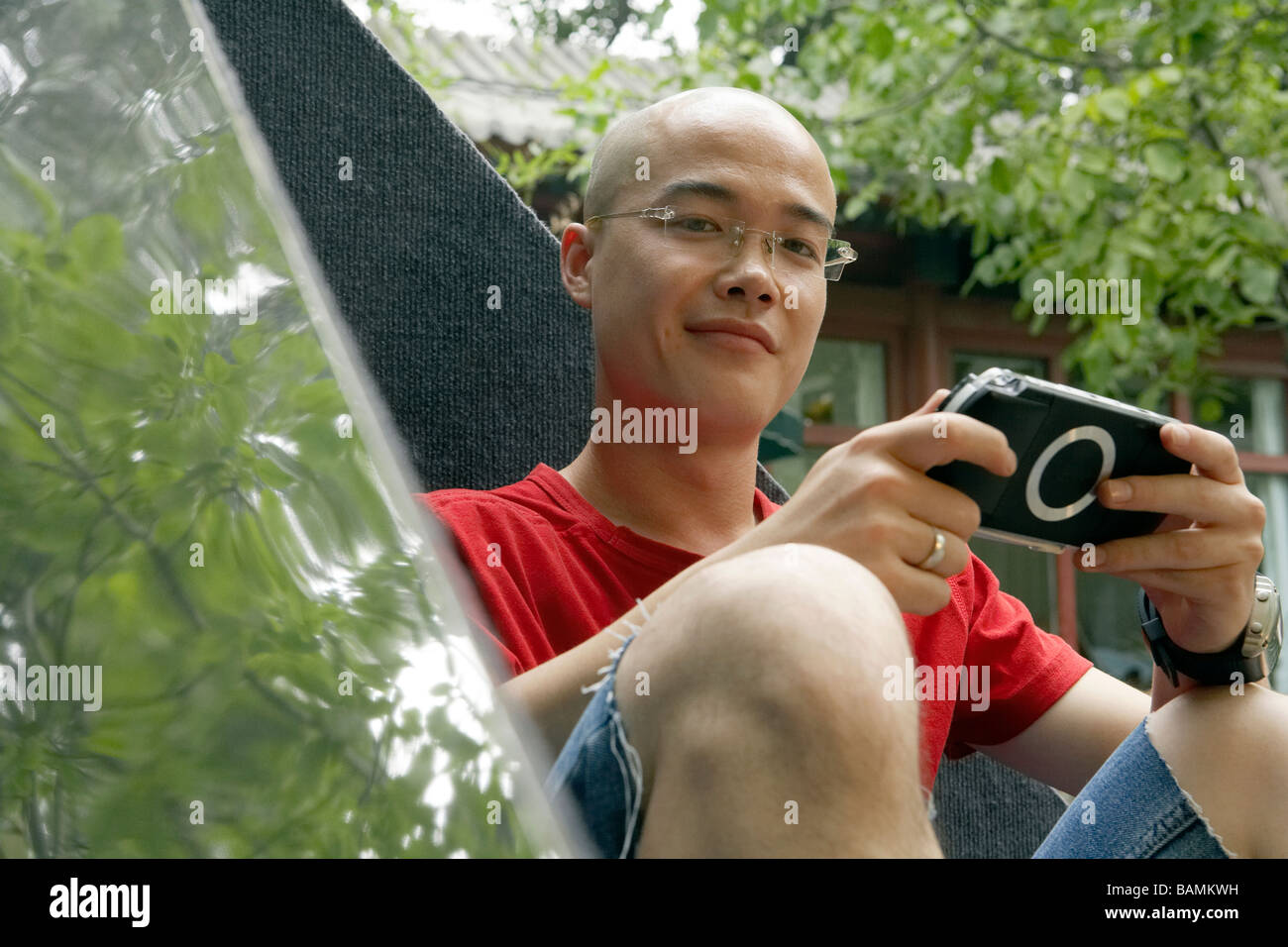 Young Man Leaning Against Sculpture Playing A Video Game And Looking At The Camera Stock Photo