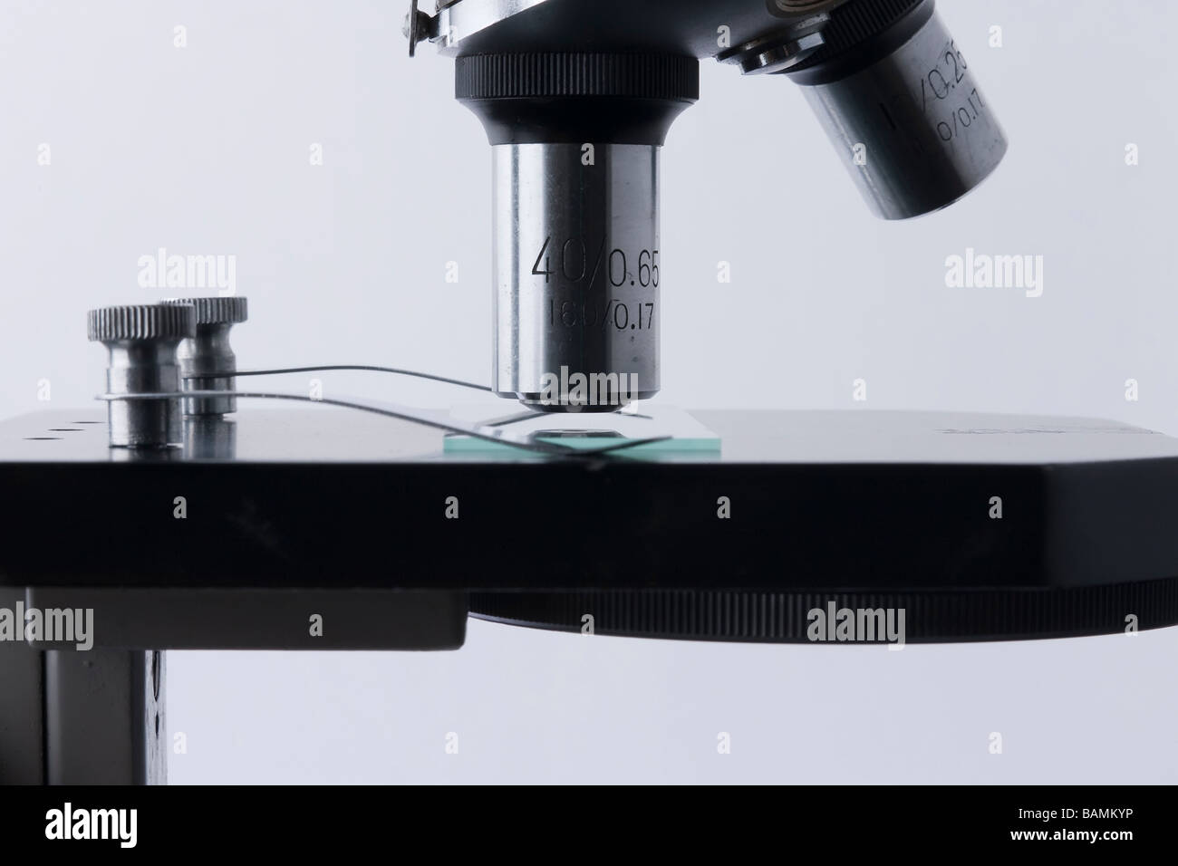 Side detail view of microscope showing objective lenses, specimen slide and retaining clips. Stock Photo