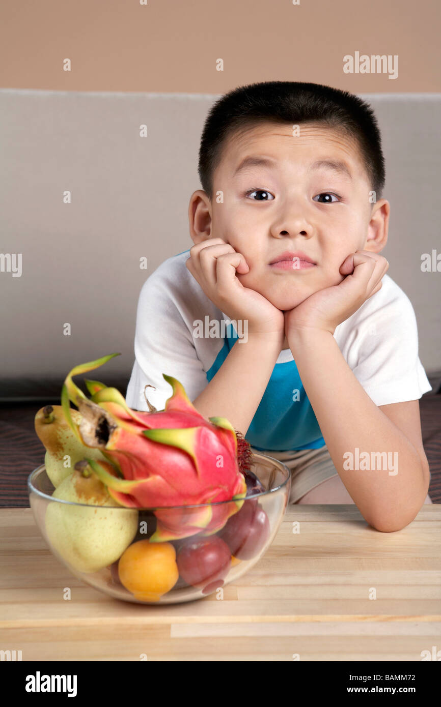 Chinese Elementary Aged Boy Leaning On A Table Next To A Bowl Of Fruit