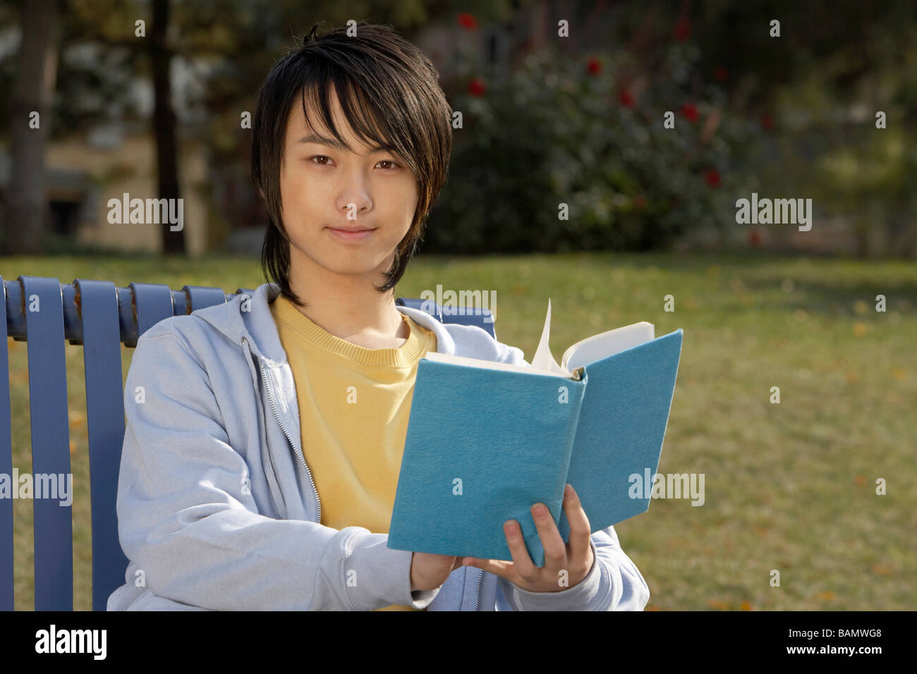 Young Man Sitting On Park Bench Reading Book Stock Photo - Alamy