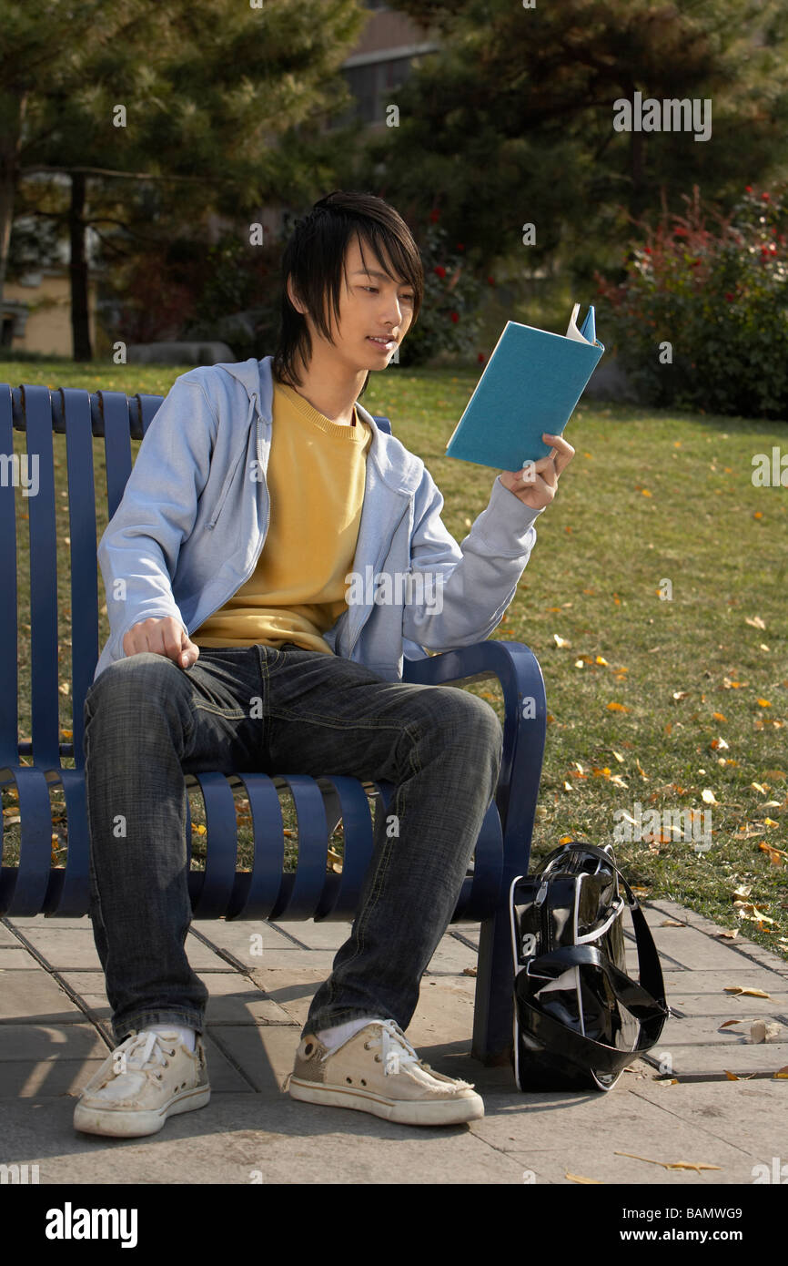 Young Man Sitting On Park Bench Reading Book Stock Photo - Alamy