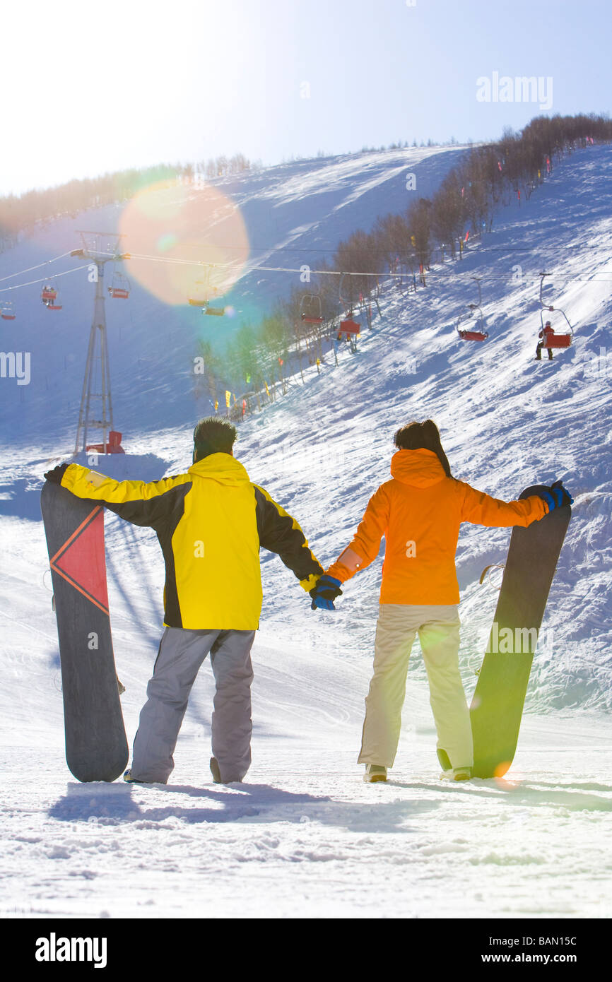 Rear view of a young man and young woman posing with their snowboards ...