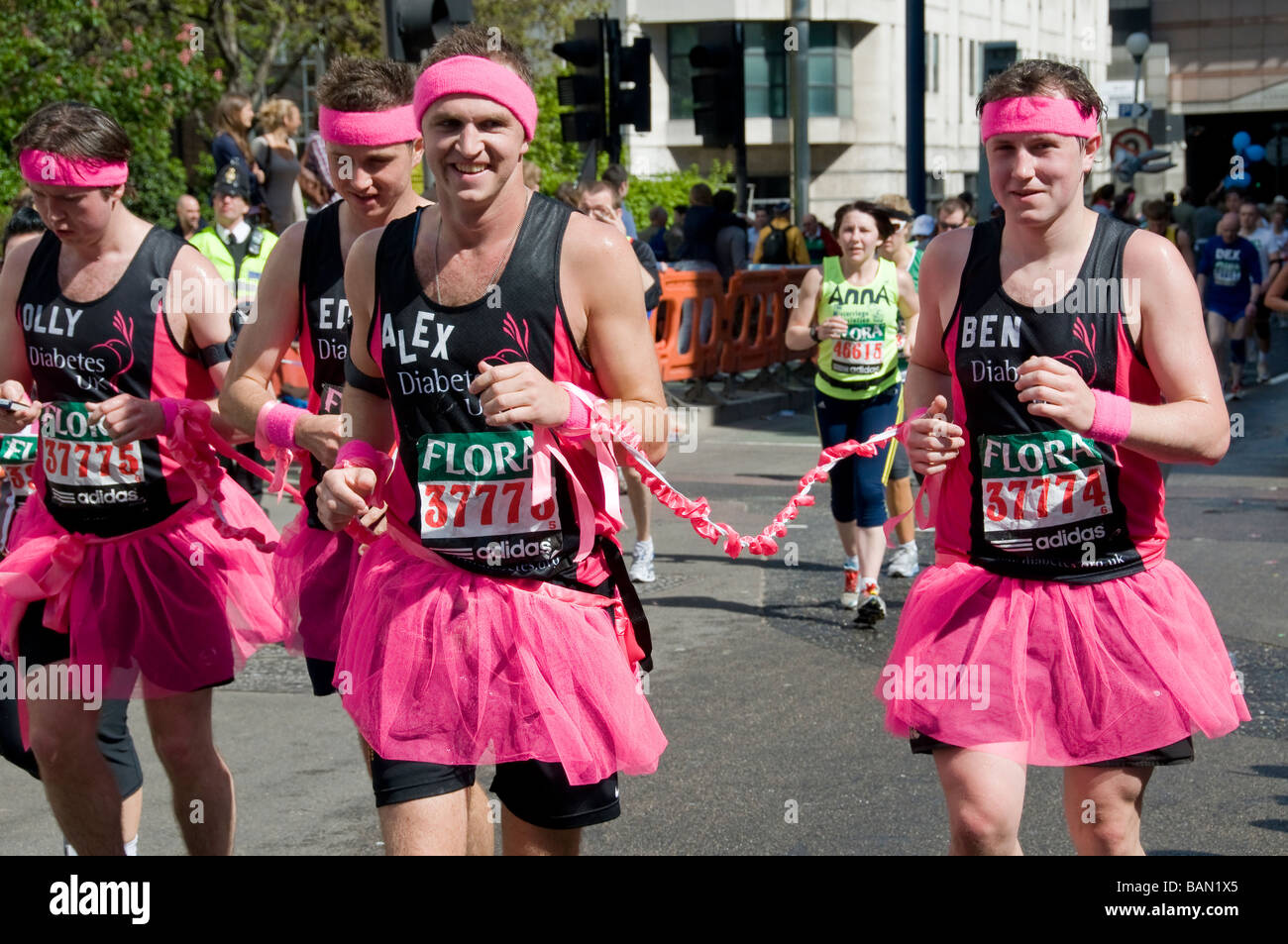 Four young men wearing pink tutus and headbands, running at London