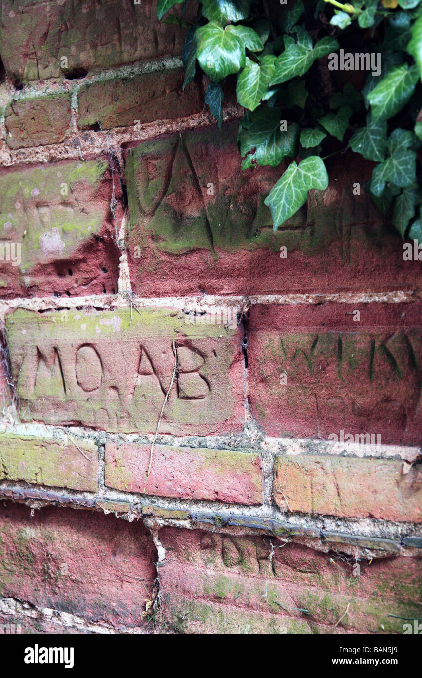 An old red sandstone wall with words cut into the surface and ivy growing on it Stock Photo