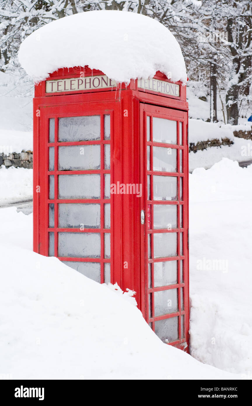 A red telephone box in deep snow by the roadside in the village of Crathie, outside Balmoral Castle, Scottish Highlands. Stock Photo