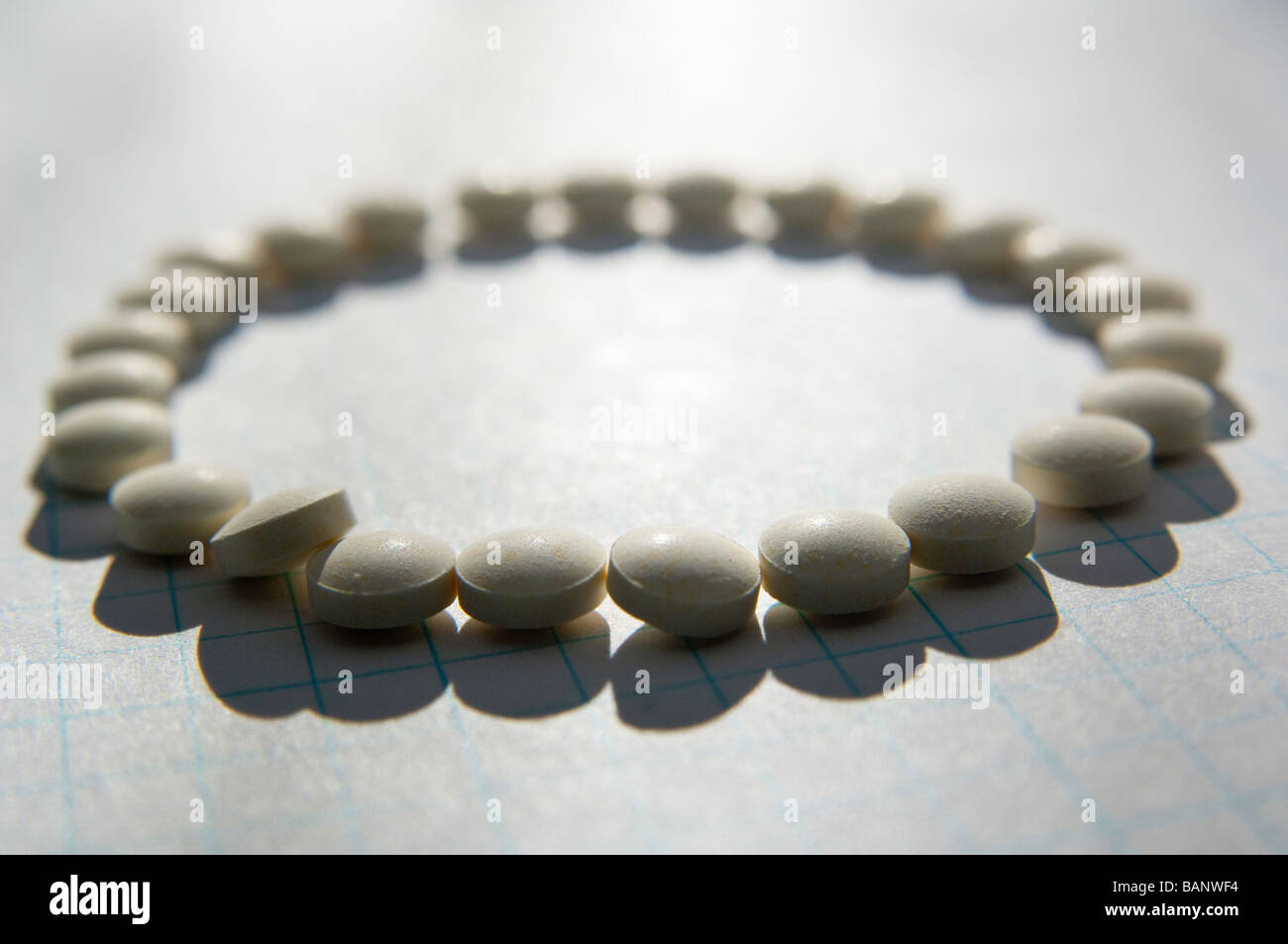 Pills on graph paper aligned to form a circle with one pill leaning on others. Stock Photo