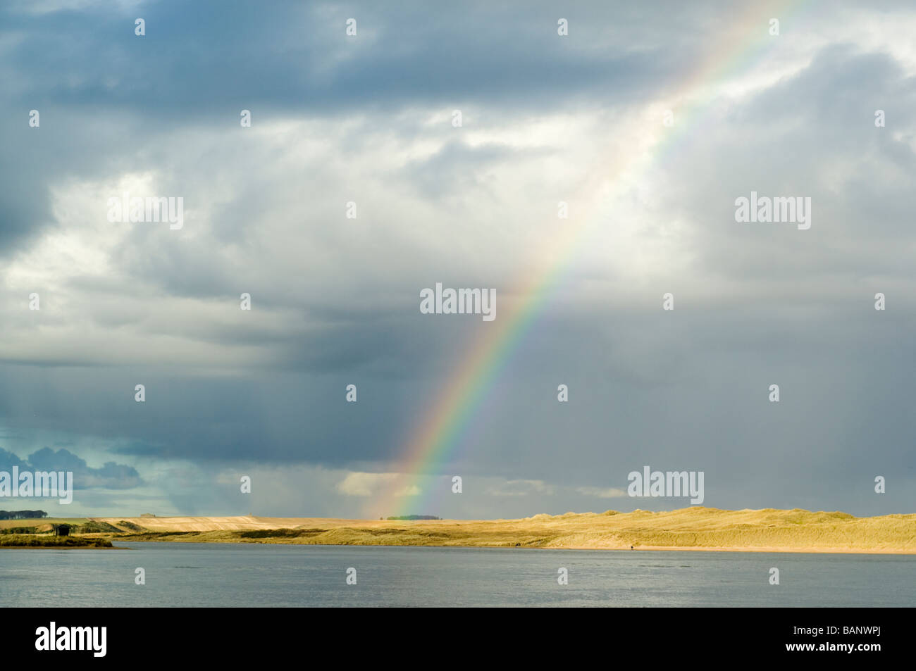 Rainbow and storm clouds over the Sands of Forvie sand dunes, viewed across the Ythan estuary. Stock Photo